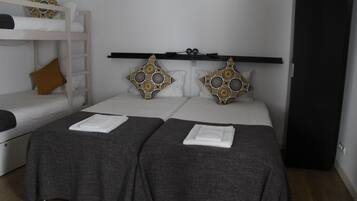 Quarto com duas camas de solteiro, uma cama beliche e uma prateleira sobre as camas.