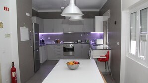 A modern kitchen with grey cabinets, a white dining table, and a red chair. - StayInn City - Évora (Évora)
