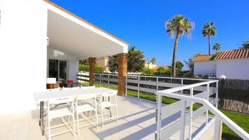 Een terras met een witte tafel en stoelen, een witte balustrade en palmbomen op de achtergrond.