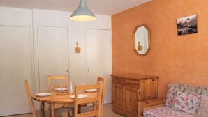 Une pièce chaleureuse avec une table à manger en bois, dressée pour quatre personnes, un canapé recouvert d’un tissu à motifs floraux et un miroir accroché au mur.