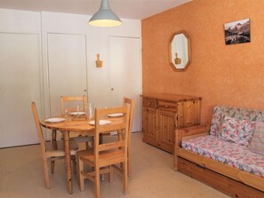 Um quarto acolhedor com uma mesa de jantar de madeira posta para quatro pessoas, um sofá com tecido floral e um espelho na parede.