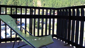 Un balcon avec une chaise verte, une vue sur une montagne boisée et un parking en arrière-plan.
