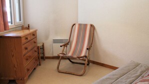Une pièce comprenant une commode en bois, une chaise à rayures, un lit et une fenêtre avec des rideaux.
