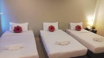 A hotel room with three single beds, each with white bedding and a red decorative pillow.