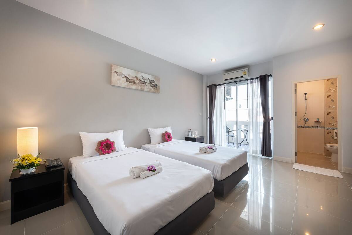 Une chambre d’hôtel avec deux lits, une table de chevet avec une lampe, un tableau au mur et une salle de bain avec douche et toilettes.