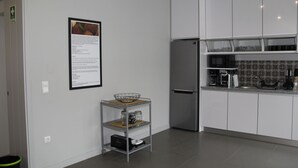 A modern kitchen with white cabinets, a stainless steel refrigerator, and a small island with a basket and jars. - StayInn City - Póvoa de Varzim (Povoa De Varzim)