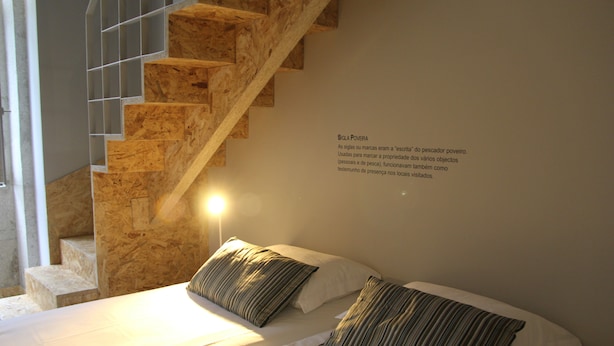 A hotel room with a wooden staircase, a bed with striped pillows, and a wall-mounted text about 'Siga Povera'. - StayInn City - Póvoa de Varzim (Povoa De Varzim)