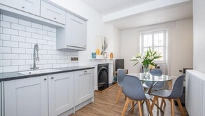 A modern kitchen with white cabinets, a black countertop, and a dining area with a glass table and grey chairs. - The Langley at 52 Old Elvet (Durham)