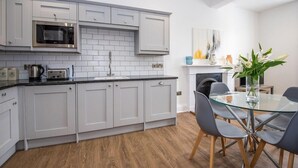 A modern kitchen with white cabinets, a microwave, and a glass dining table with chairs. - The Langley at 52 Old Elvet (Durham)