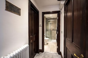 Ein Flur, der zu einem Badezimmer mit Dusche, Toilette und einem Heizkörper an der Wand führt.