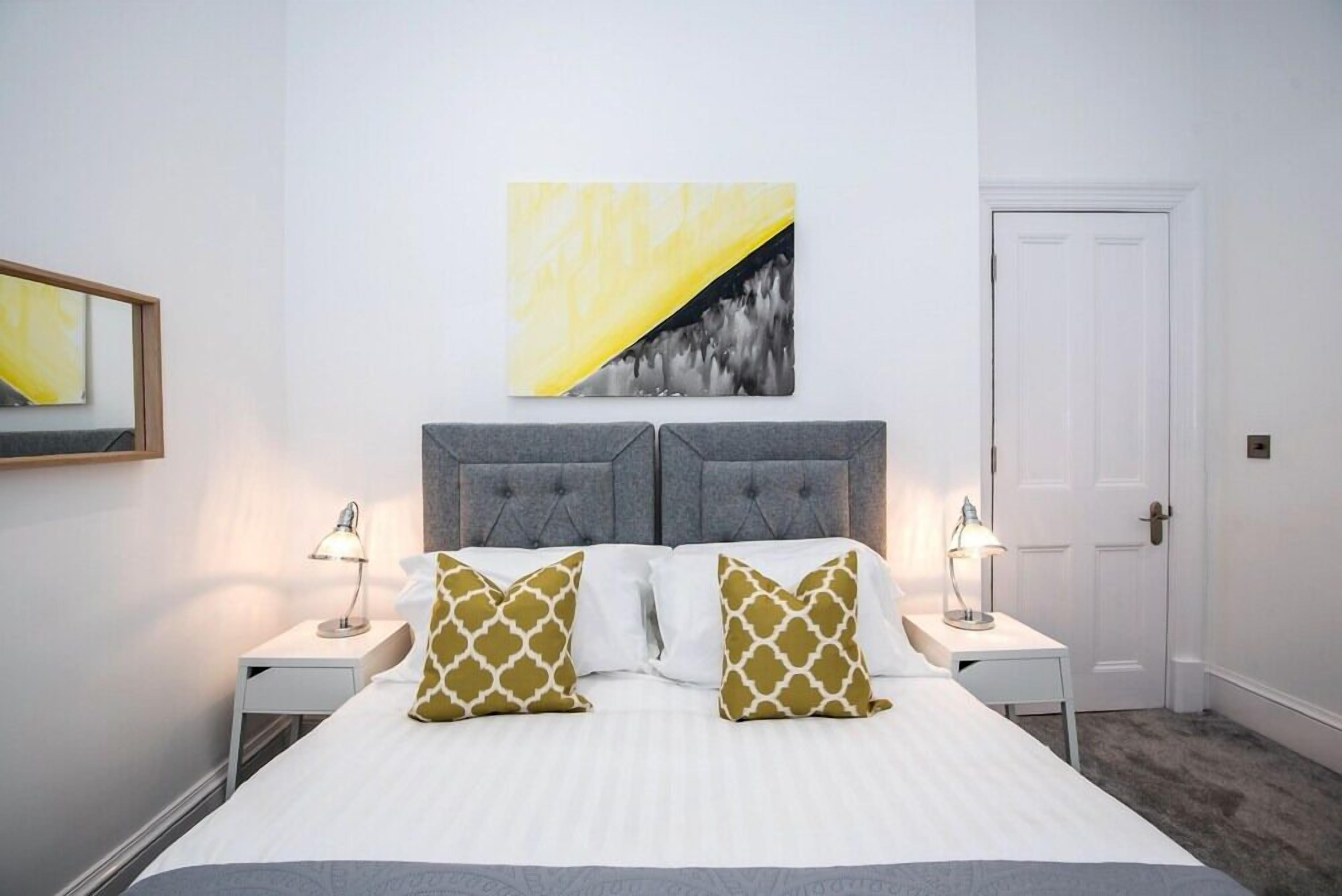 A neatly arranged bedroom with a large bed, two bedside tables with lamps, a grey upholstered headboard, and a white door.