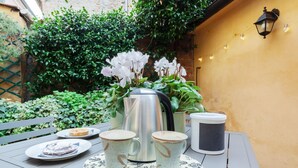 A table with a teapot, cups, and plates, surrounded by greenery and a yellow wall.