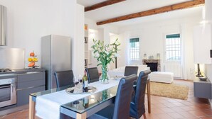 A modern kitchen with a dining area, featuring a glass table, chairs, and a vase with flowers.
