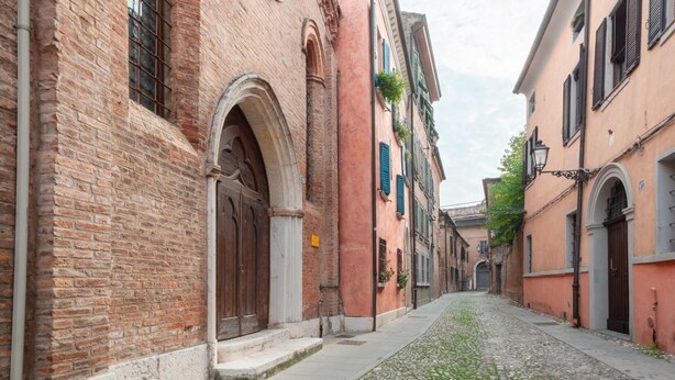 A cobblestone street flanked by historic buildings with arched doorways and windows.