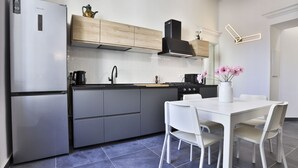 A modern kitchen with a refrigerator, stove, and white dining table with chairs. - GuestHost - Garibaldi huge and cozy apartment (Napoli)