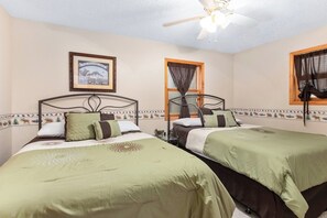 A room with two beds, a ceiling fan, a framed picture on the wall, and a window with curtains.