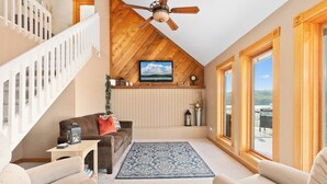 A spacious living area with a wooden ceiling, a television, a comfortable sofa, and a large window offering a view.
