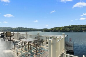 A deck with outdoor furniture, a railing, and a view of a lake and forest.