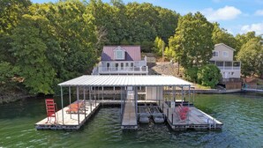A houseboat with a covered deck, a small porch, and a dock extending into a body of water.