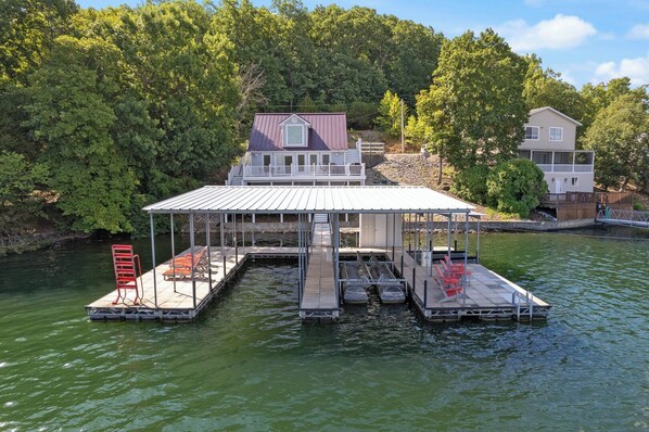 A houseboat with a covered deck, a small porch, and a dock extending into a body of water.