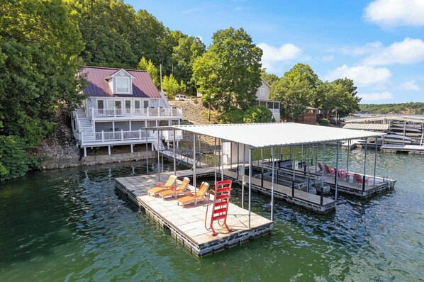 A dock with a covered area, lounge chairs, and a house in the background.