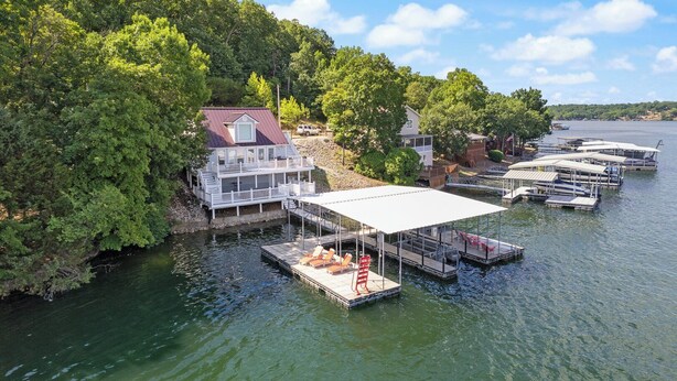 A lakeside house with a dock, boats, and a covered area with lounge chairs.