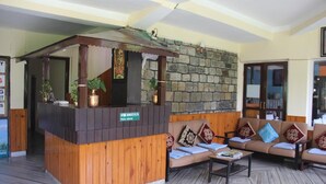 Zona de recepción con mostrador de madera, pared de piedra y sofá con cojines estampados.