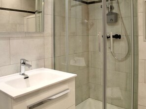 Un bagno moderno con doccia vetro, lavandino bianco e specchio.