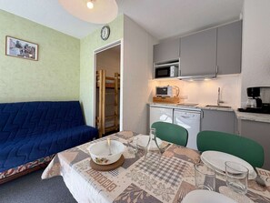 Un ambiente compatto con angolo cottura, un tavolo da pranzo per due persone, un divano blu e un letto piccolo.