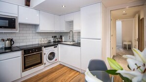 Una cocina moderna con armarios blancos, microondas, horno y lavadora.
