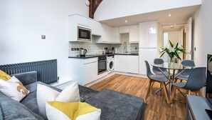 Una cocina moderna con armarios blancos, un microondas y un horno empotrado. Hay un comedor con una mesa de vidrio y sillas.