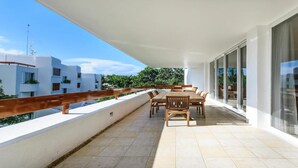 Un balcon avec une table et des chaises pour prendre les repas, de grandes fenêtres et une vue sur les bâtiments voisins.