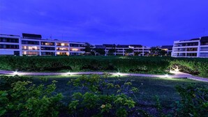 Un hôtel moderne à plusieurs étages, doté d’un éclairage extérieur et d’un jardin bien entretenu.