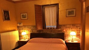 A hotel room with a large bed, two bedside tables with lamps, a window with a curtain, and a brick-patterned wall. - Ca' Le Rose (Bagnolo San Vito)