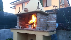 A brick outdoor pizza oven with a fire burning inside, a yellow bucket, and a white bucket with a metal handle. - Ca' Le Rose (Bagnolo San Vito)