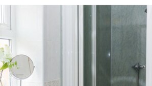 Une salle de bain avec une porte de douche en verre, un miroir rond et une plante en pot.