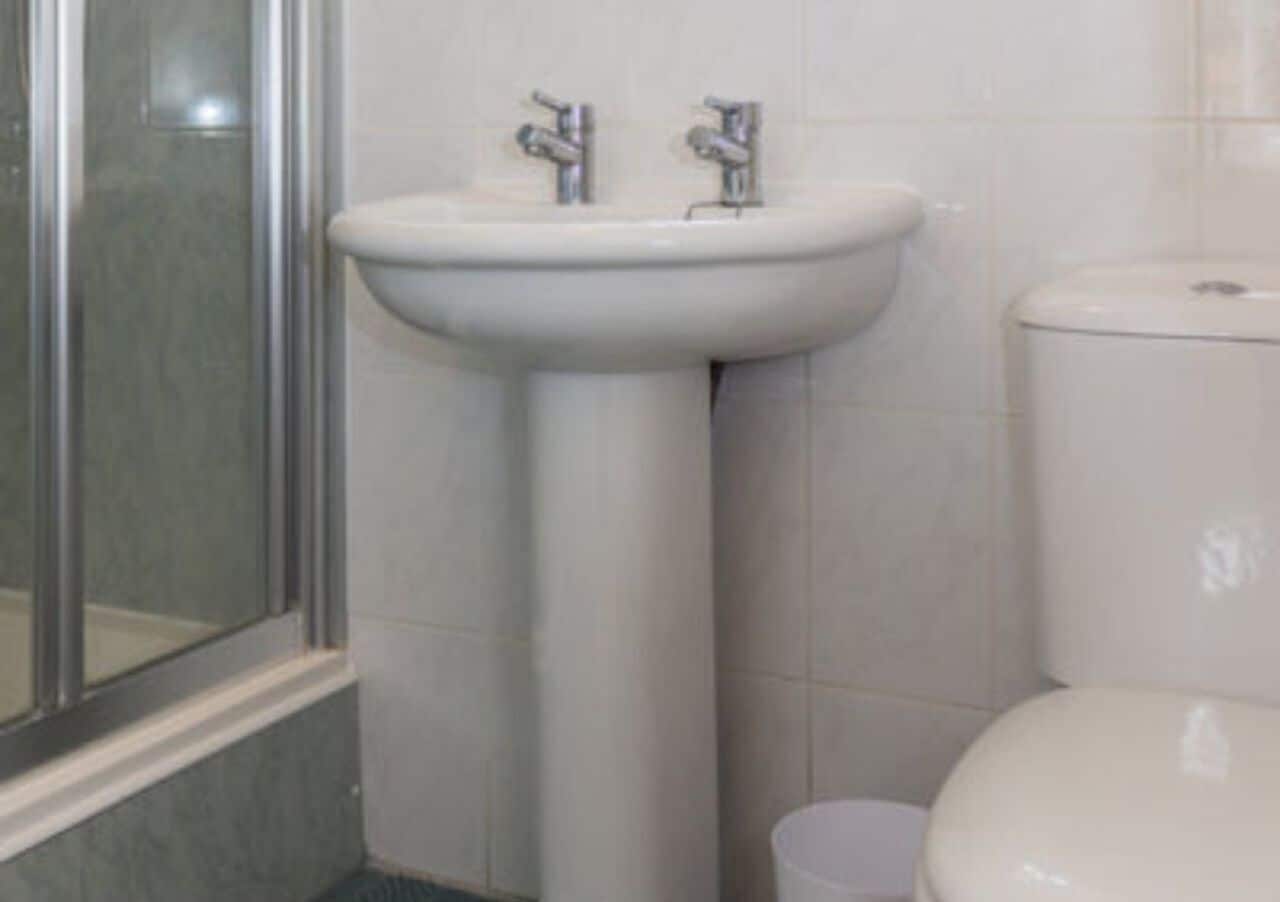 Baño con lavamanos pedestal, inodoro y cabina de ducha de vidrio.