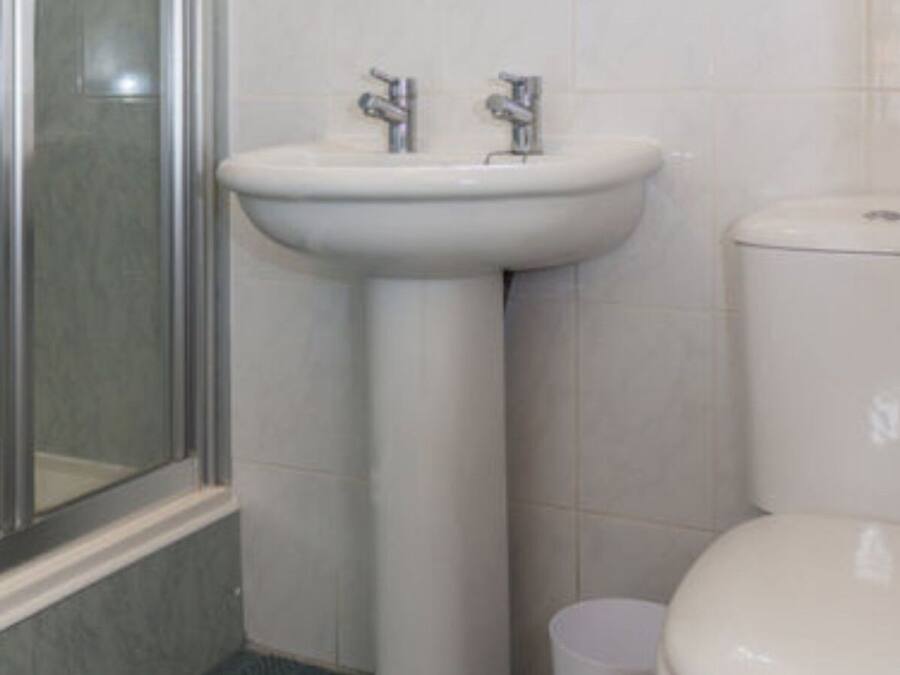 Baño con lavamanos pedestal, inodoro y cabina de ducha de vidrio.