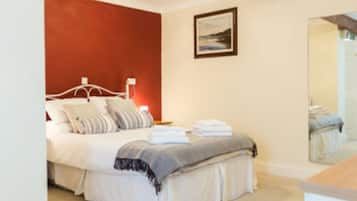 A bedroom with a bed, pillows, a bedside table, a lamp, a mirror, and a framed picture on the wall.