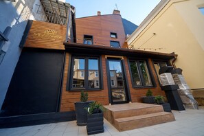Un hotel moderno con fachada de madera, ventanas amplias y un pequeño espacio de asientos al aire libre.