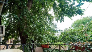 Um deck de madeira com uma cadeira e uma mesa, cercado por guarda-corpo de metal e vegetação exuberante.