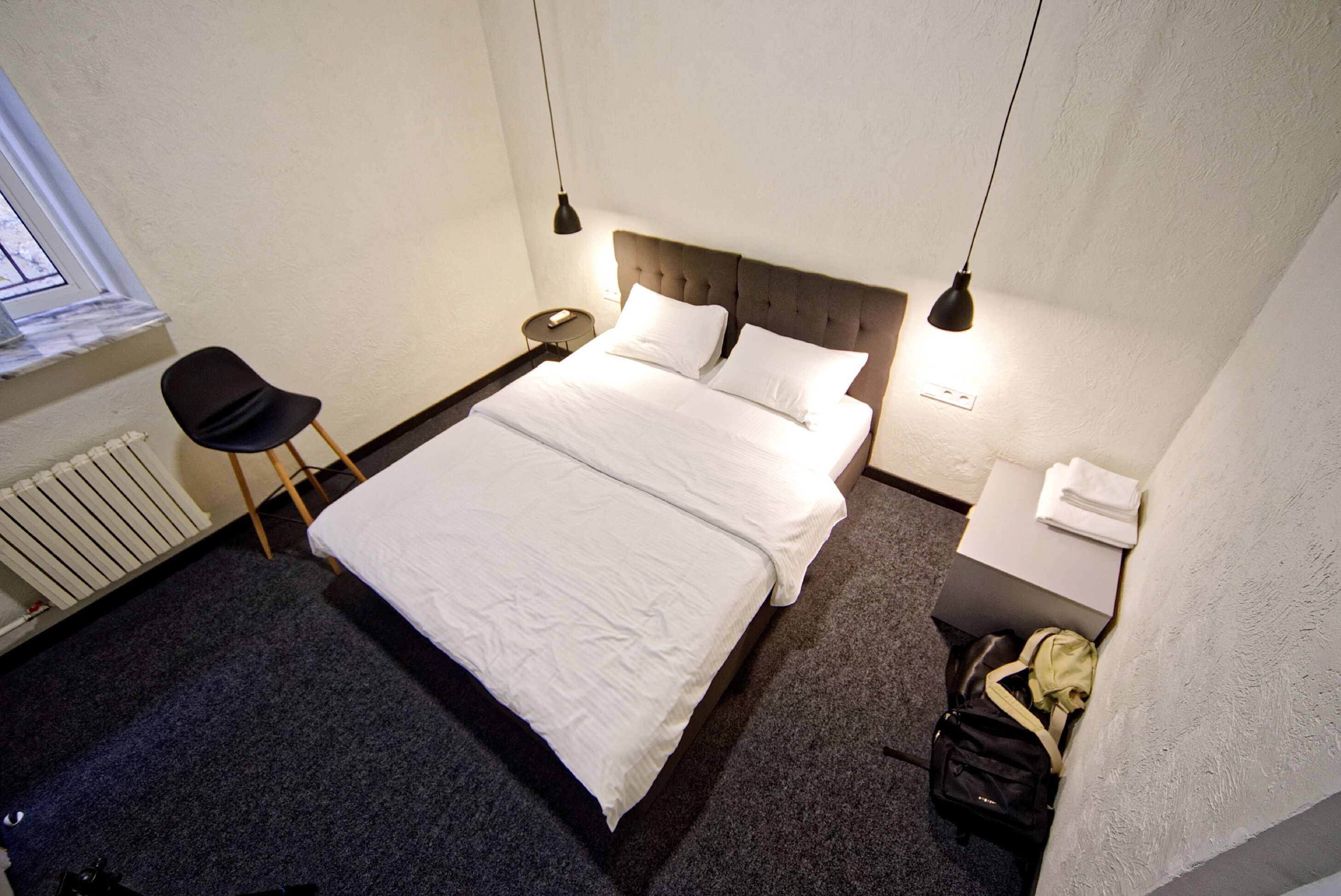 A hotel room with a large bed, a chair, a small table, and a suitcase.