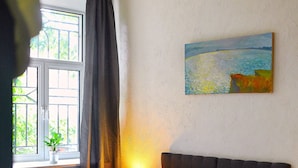 Quarto com cama, janela com cortinas, um quadro na parede e abajur.