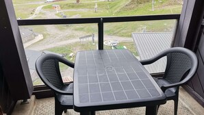 Un balcon avec une table et deux chaises, donnant sur une voie ferrée et un paysage verdoyant.
