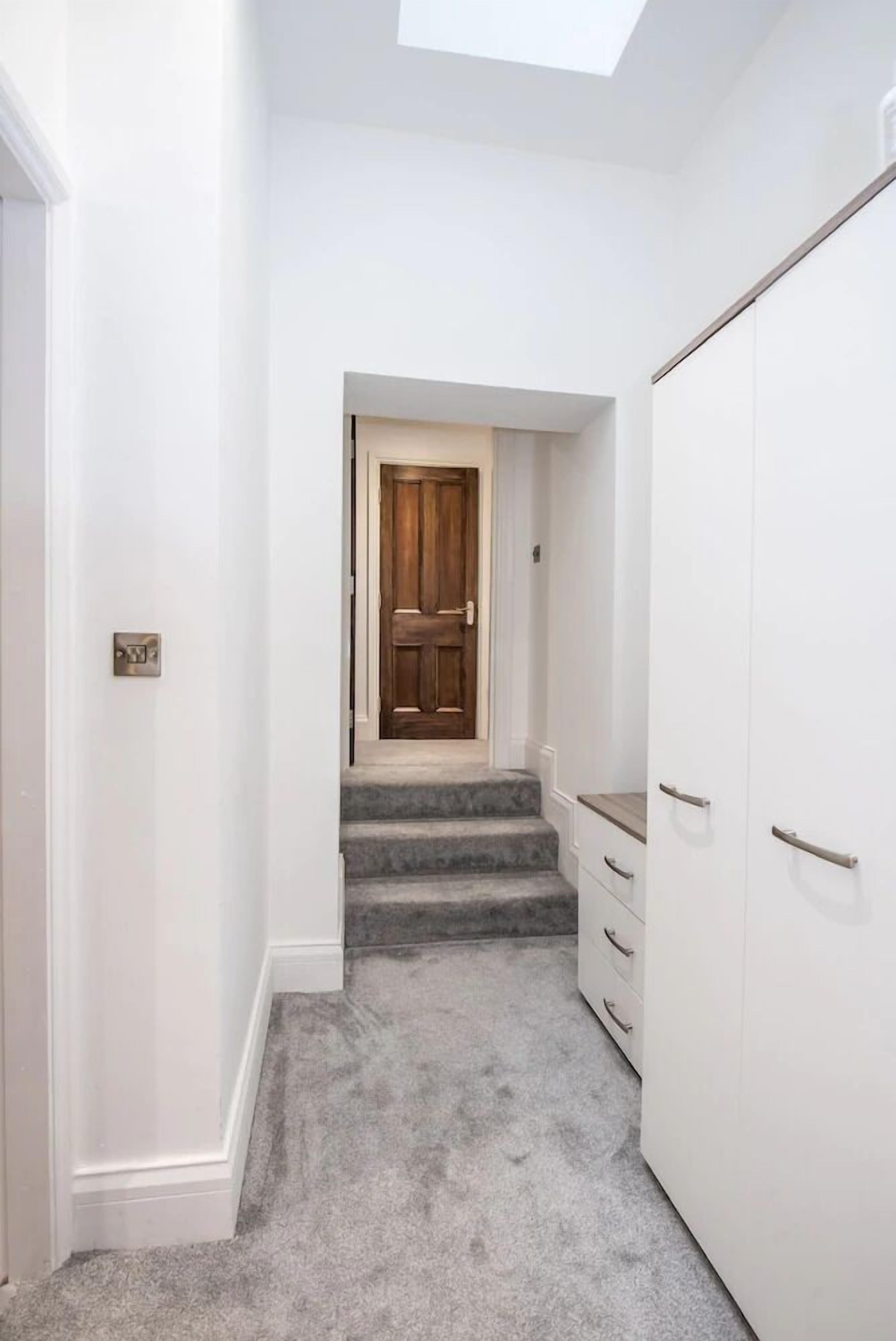 A narrow hallway with a carpeted floor, a wooden door at the end, and a white wardrobe on the right.