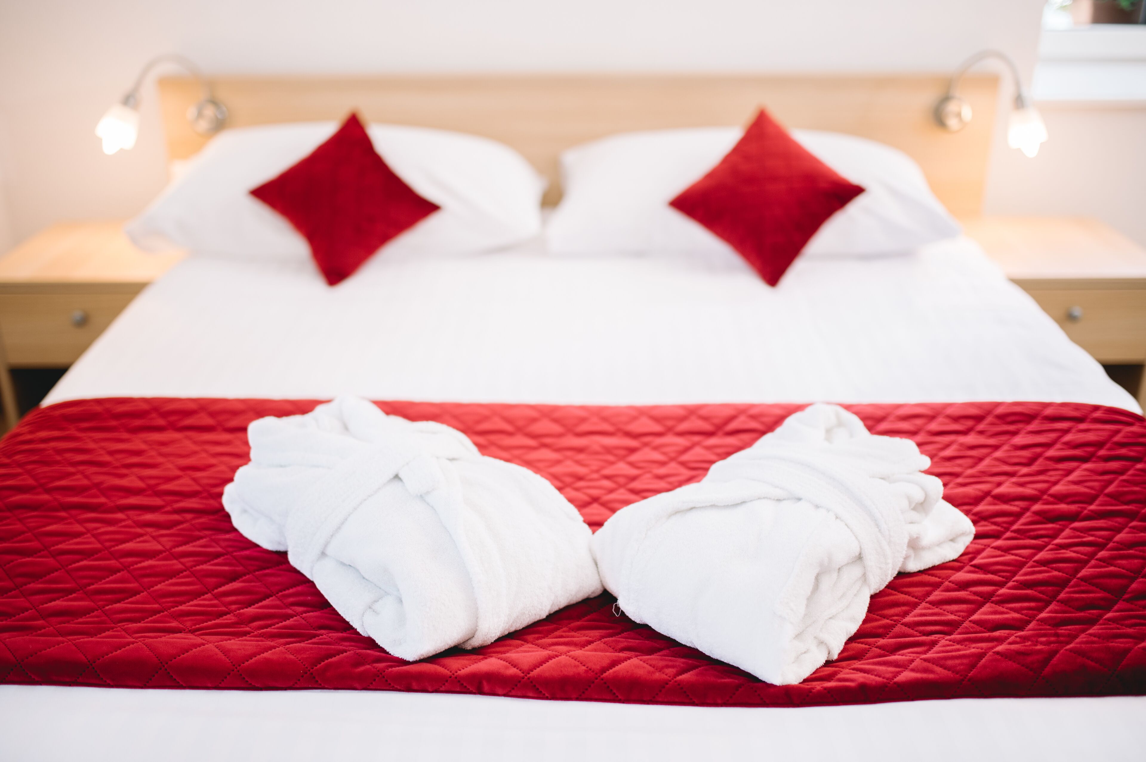 Un lit bien fait, recouvert d’une couverture rouge et agrémenté de deux serviettes blanches.