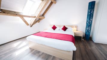 Un dormitorio moderno con techo inclinado, estructura de cama de madera, ropa de cama blanca y una almohada roja de acento.
