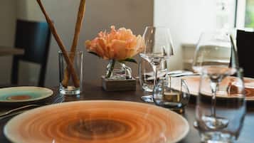 A dining table set with plates, glasses, and a vase with a flower.