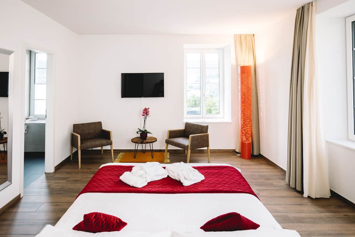Een hotelkamer met een groot bed, twee fauteuils, een televisie en een raam met gordijnen.