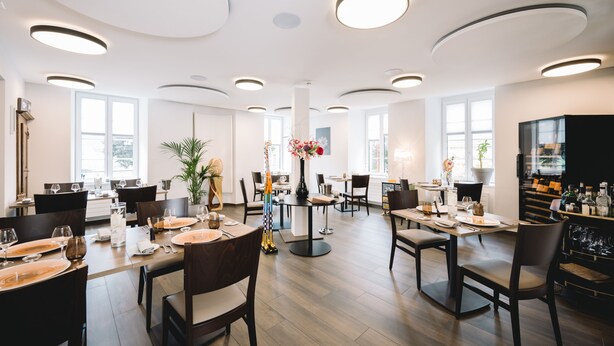 Een modern restaurant met ronde tafels, donkere stoelen en een decoratieve vaas in het midden.